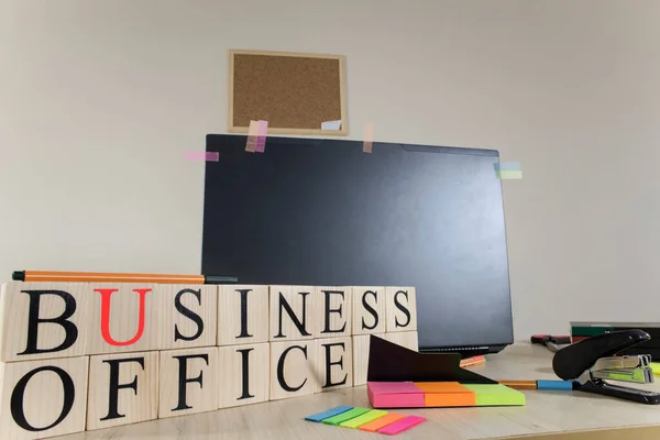 Text of business office on wooden cubes in front of office desk. There are laptop and office supplies on the table. Consept and studio.