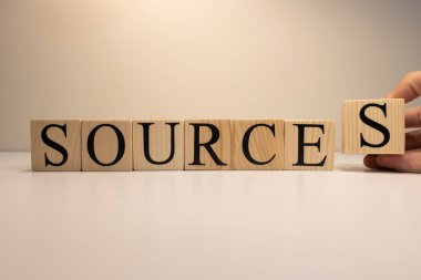 Kaynaklar ahşap küplerden mesaj gönderiyor. Beyaz bir arka planda. Bir el S harfini tutuyor..