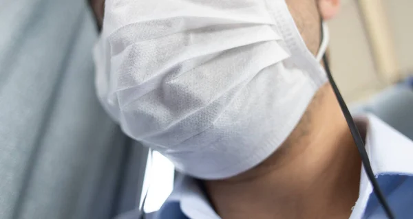 Ağzında beyaz sağlık maskesi olan bir adam..