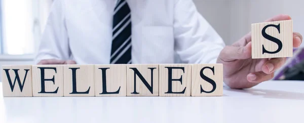 The word wellness from wooden cubes. Man in shirt and tie on the background.