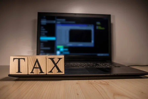 The laptop screen on the table is open. Tax word on wooden cubes on laptop. Photographs were taken in the spotlight.
