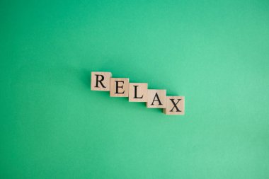 Tahta küplerden yapılmış gevşeme kelimesi. Arka plan yeşil ve stüdyoda çekilmiş. Dinlenme ve sakinleşme kavramı.