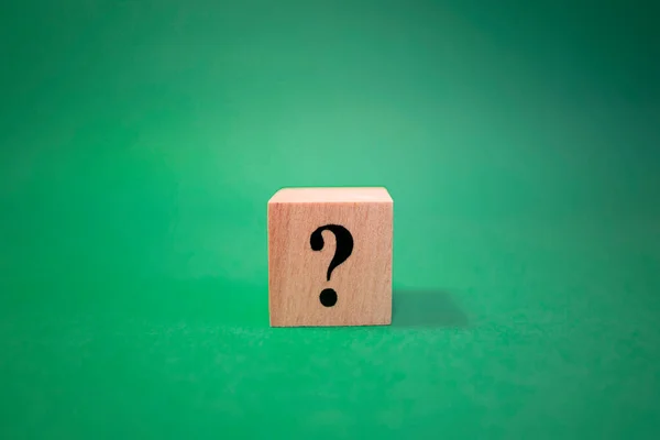 The word question mark made of wooden cubes. The background is green and photographed in the studio