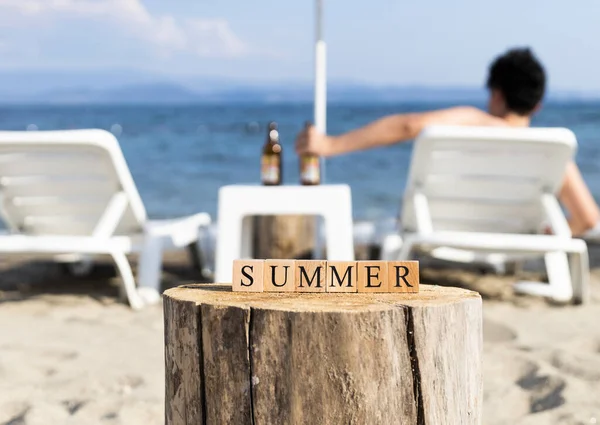 木製のキューブで作られた日の単語 ビーチの砂の上でクローズアップ 夏の日に撮影 サングラスと日焼け止めとスリッパがあります — ストック写真