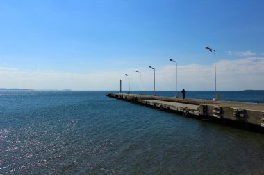 Deniz kenarı ve beton iskele. İskelede yürüyen bir adam. Fotoğraf açık havada güneşli bir havada çekildi. Akcay, Türkiye.
