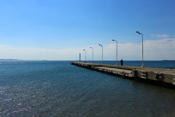 Seaside and concrete pier. A man walking on the pier. Photo was taken in sunny outdoors. Akcay, Turkey.