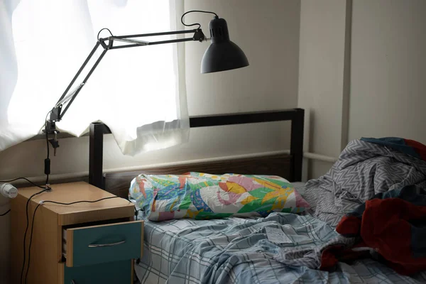 Düzensiz tek kişilik yatak odası. Yalnız bekar bir adam. Pencerenin yanında bir masa lambası var. Gün boyunca fotoğraflanmış..