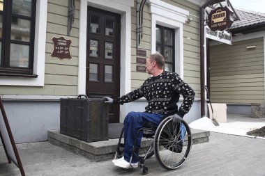 Minsk, Belarus, 19 Eylül 2016 - Tekerlekli sandalyedeki bir adam girişteki yüksek veranda ve rampa olmadığı için giremediği bir mağazanın kapısına bakıyor