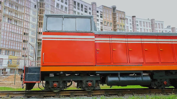 Kırmızı buharlı lokomotif yeni bir şehir bölgesindeki tren istasyonunu geçiyor.