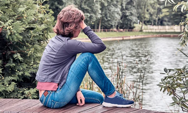 Kadın bankta oturuyor ve sonbahar parkındaki göle bakıyor.