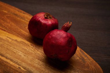 Koyu kahverengi ahşap masa üzerinde dokulu orta altın tonahşap doğrama tahtası üzerinde iki koyu kırmızı nar, yukarıdan vurdu. Yukarıdan yumuşak sıcak ışık. Punica granatum.