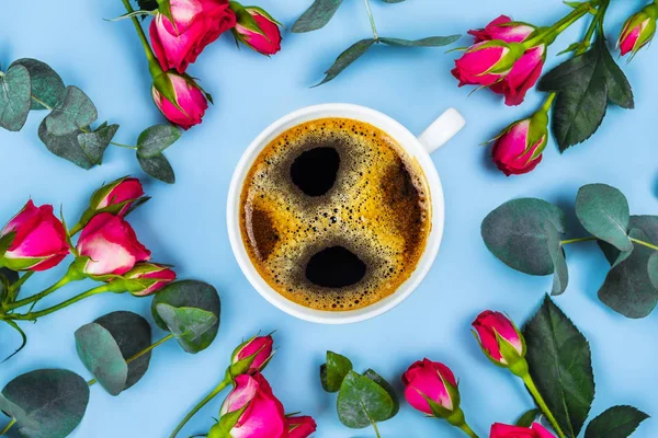 Ranní šálek kávy a nádherné růže se šanky eukalyptu na modrém pozadí, pohled shora. — Stock fotografie