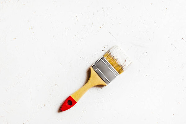 Construction brush with red handle on painted white plywood.