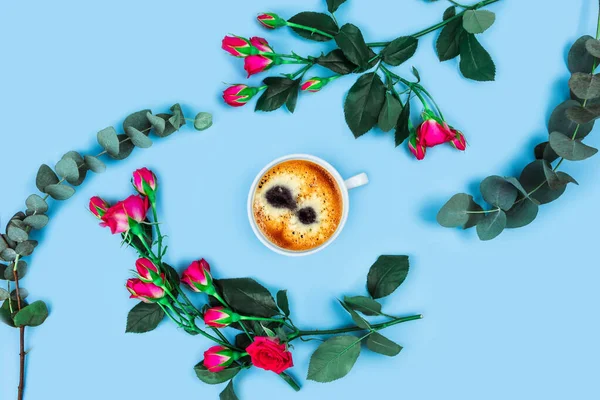 Ranní šálek kávy a krásné růže s prameny eukalyptu na modrém pozadí. — Stock fotografie