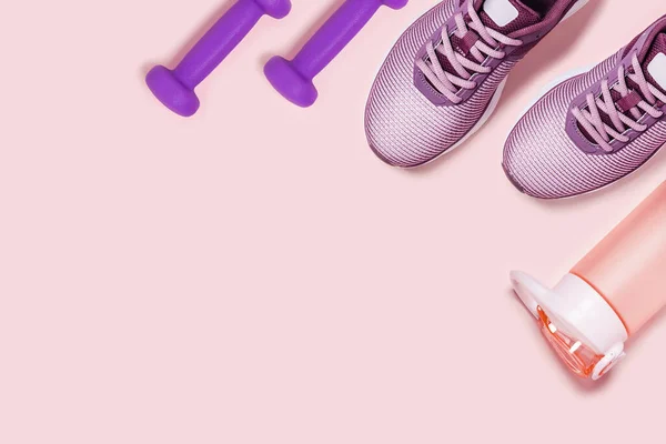 Pembe arka planda spor ayakkabılar, dambıllar ve titretici..