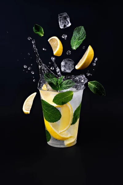 Buz küpleri, limon dilimleri ve limonata bardağına sıçrayan nane yaprakları. Siyah arkaplan