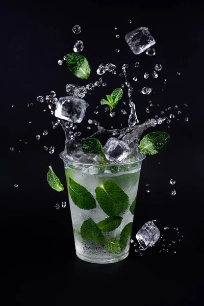 Buz küpleri ve nane yaprakları limonata bardağına sıçrıyor. Siyah arkaplan