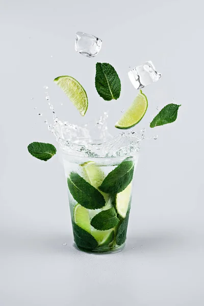 Buz küpleri, limon dilimleri ve limonata bardağına sıçrayan nane yaprakları. Açık gri arkaplan