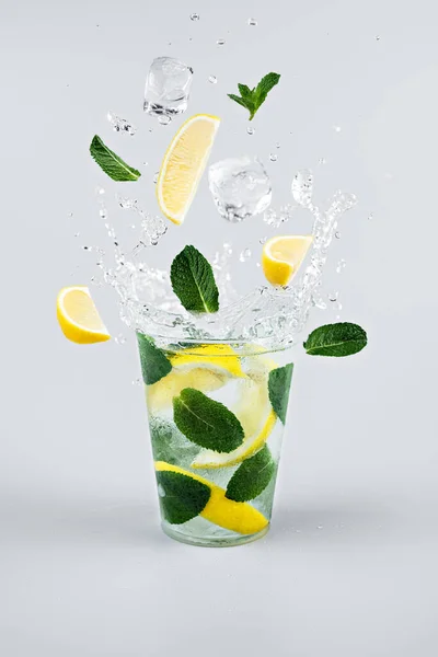 Buz küpleri, limon dilimleri ve limonata bardağına sıçrayan nane yaprakları. Açık gri arkaplan