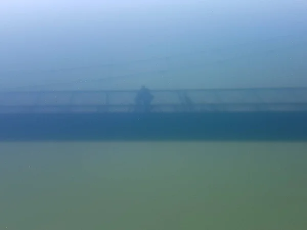 Blue-green water and the shadow of a bridge on the water Man on the bridge.