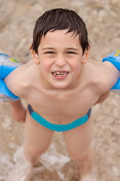 Süt dişli çocuk plajda şişme kolluk takıyor.
