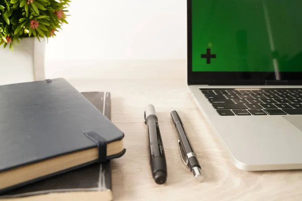 Open laptop with green screen, books and pen. All with isolated screen on wooden desk.