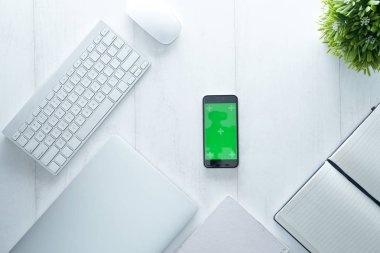 Not defteri, akıllı telefon, saat, fare, klavye ve malzemelerle dolu ofis masası, beyaz ahşap masaya izole edilmiş. Kopyalama alanı olan üst görünüm, beyaz, temiz, düz uzanma.