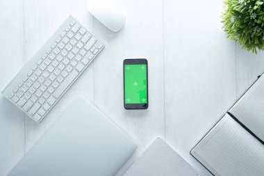 Not defteri, akıllı telefon, saat, fare, klavye ve malzemelerle dolu ofis masası, beyaz ahşap masaya izole edilmiş. Kopyalama alanı olan üst görünüm, beyaz, temiz, düz uzanma.