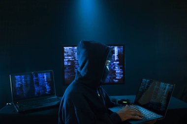 Masadaki verileri çalmak için birden fazla bilgisayar kullanan bir hackerın arka görüntüsü
