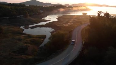 Etrafında tepeler ve asfalt yollar olan gölün üzerinde güzel bir gün doğumu manzarası var..