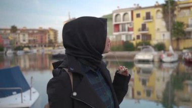 Siyah tesettürlü genç Asyalı kadınların güzel gülümsemesi Saplaya limanının manzarasının keyfini çıkarıyor.