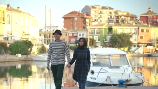 幸せなアジアのカップルはカラフルな家の背景と川の近くに手をつないで歩く — ストック動画