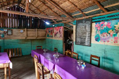 Andavadoaka, Madagaskar-13 Ocak, 2019: bir menü bir duvar üzerinde bir tahta üzerine yazılmış, Ahşap sandalyeler ve masalar Andavadoaka, Madagaskar merkezi pazarında rustik bir restoranda.