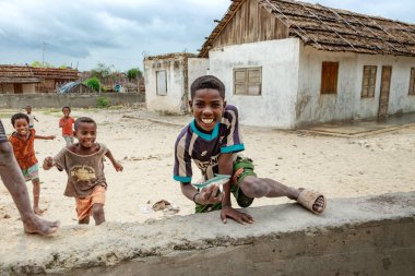 Andavadoaka, Madagascar - January 13th, 2019: Local malagasy kids running and playing next to a rustic building in Andavadoaka, Madagascar. clipart