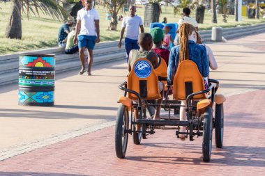 Durban, Güney Afrika-Ocak 06, 2019: Iki siyah erkek ve iki beyaz-Kafkas kız Durban, Güney Afrika plajında bir binmek için bir quadricycle paylaşımı.