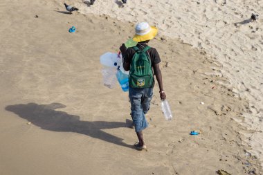 Durban, Güney Afrika-7 Ocak, 2019: Durban, Güney Afrika 'da bir plajda kum yürüyüş plastik şişeler toplayan bir Güney Afrika siyah adam.