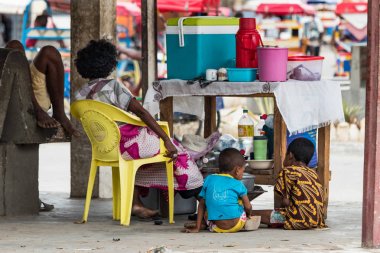Toliara, Madagaskar-10 Ocak, 2019: Toliara, Madagaskar yerel pazarında karşı açık havada olarak ahşap bir masa ile çay ve kahve satan çocukları ile bir Madagaskar anne.
