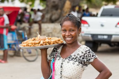 Toliara, Madagascar - January 10th, 2019: A local young malagasy woman selling Nem - eggrolls, smiling, in the streets at the market in Toliara, Madagascar. clipart