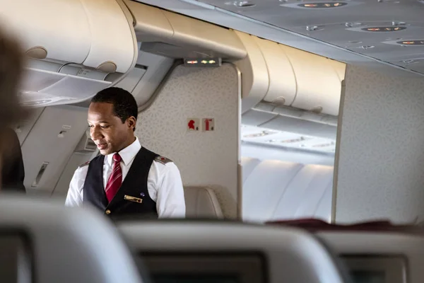Doha, Katar-20 Şubat, 2019: Qatar Airways Airbus A350 üzerinde onboard bir yolcu ile konuşan bir erkek kabin mürettebat uçuş görevlisi.