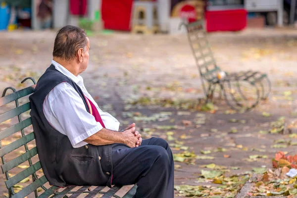 Starší muž, který sedí na lavici v parku a dívá se jinam. — Stock fotografie