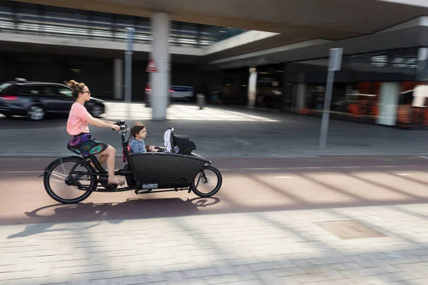 Una mujer en bicicleta con niños en una bicicleta de carga en el Amsterdam Centr —  Fotos de Stock