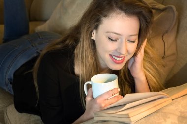 Genç kadın bir kitap okuma ve kahve sahip yüz aşağı yatıyor