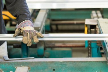 Alüminyum profilin uzantısını kontrol eden güvenlik eldivenleri kullanan bir adam..