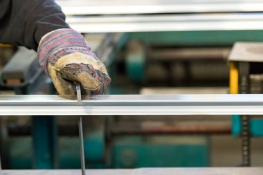 Alüminyum profilin uzantısını kontrol eden güvenlik eldivenleri kullanan bir adam..