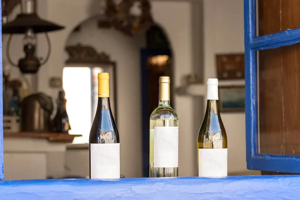 Three wine bottles with label placed next to an open wooden windows at a Greek tavern in Hydra, Greece.