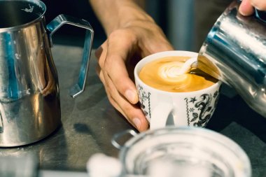 Barista eller latte sanat yapmak için bir fincan sıcak süt dökerek.