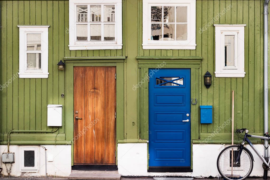 A green wooden wall with windows and two doors with post boxes on the side in Norway.