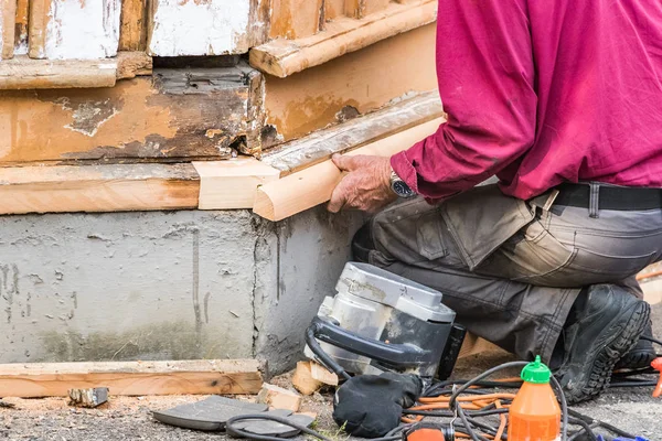 Een mannelijke timmerman gehurkt neer het assembleren van een stuk hout op een oud huis. — Stockfoto