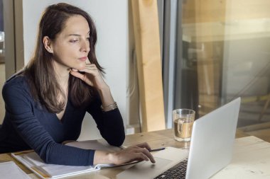 Dizüstü bilgisayarıyla çalışan bir kadın ellerini çenesine koyar..