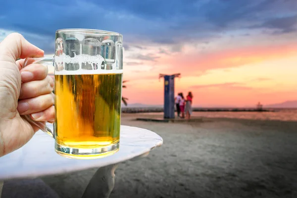 Un homme tenant un pot avec de la bière à la plage au coucher du soleil . — Photo